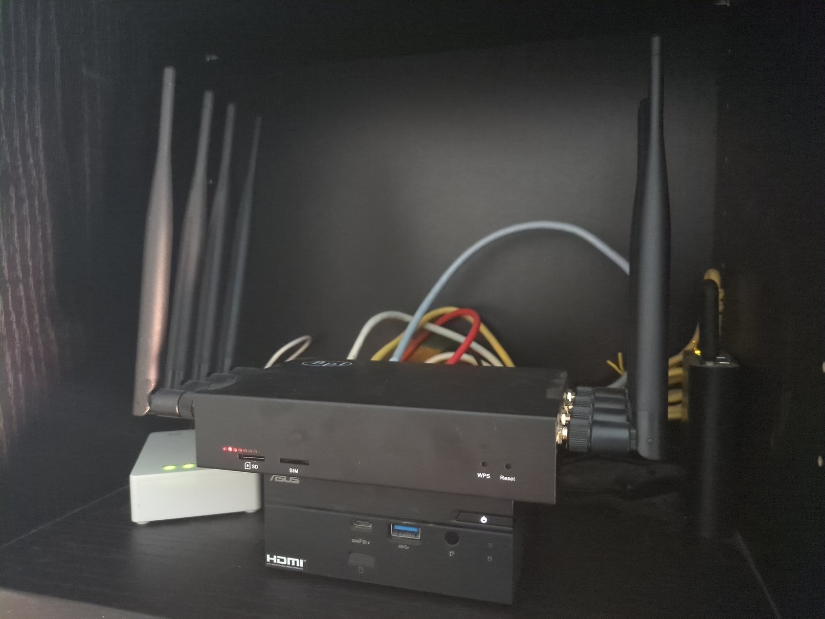 Imatge d’un prestatge amb el Mini PC ASUS PN50, que fa de servidor, i un router Banana Pi R3 a sobre. Hi ha llumetes enceses i molts cables Ethernet de diversos colors per darrere.